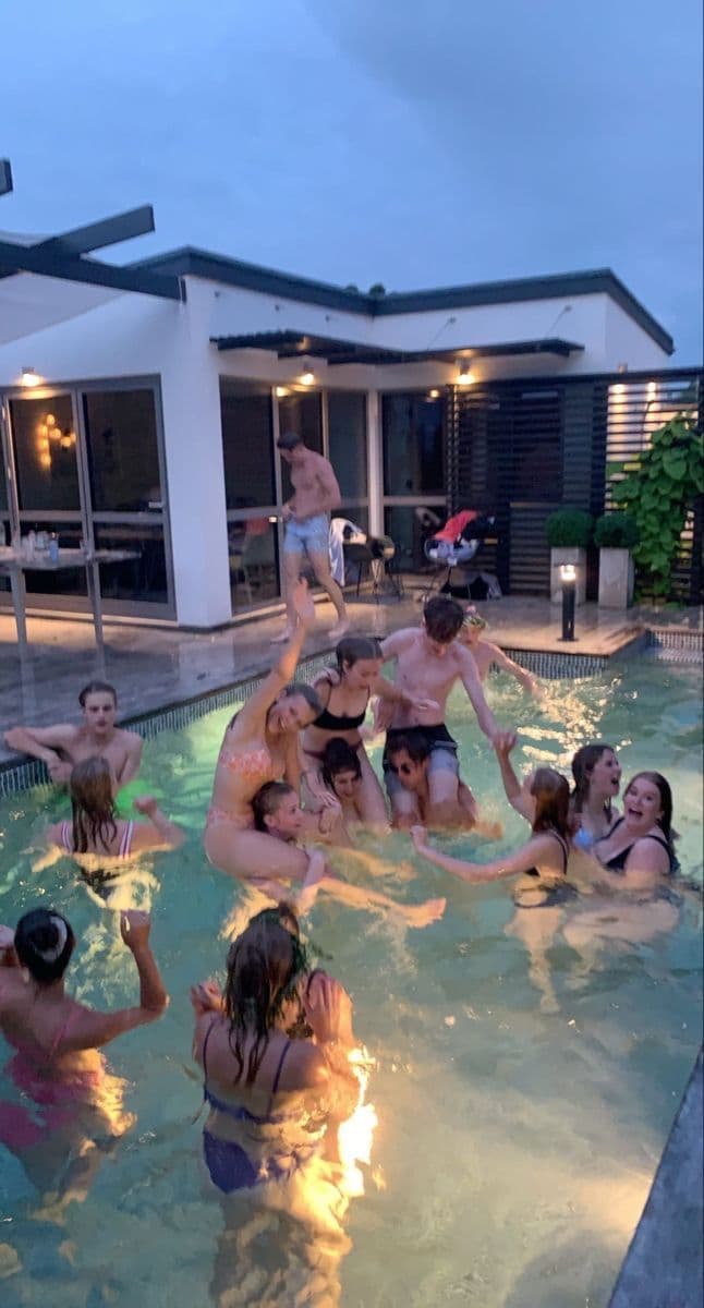 Group of friends partying together in a backyard pool at dusk