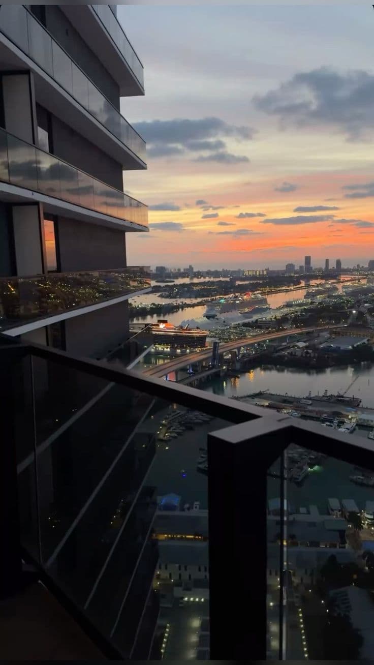 the view from an apartment balcony at sunset with boats in the water and city lights