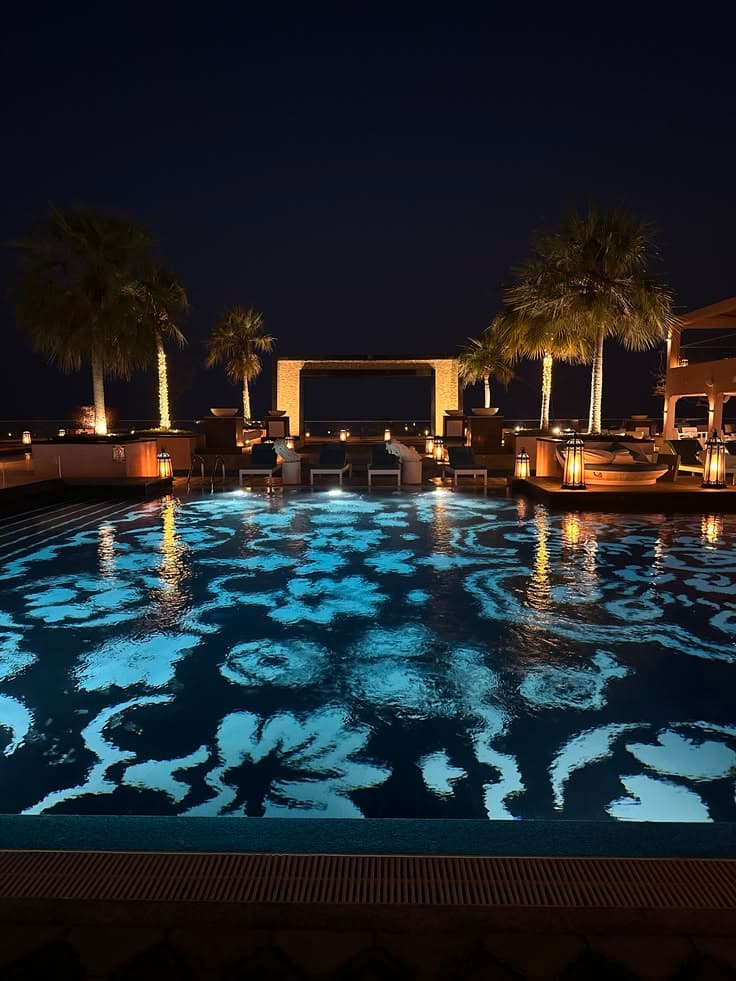an outdoor swimming pool at night with palm trees