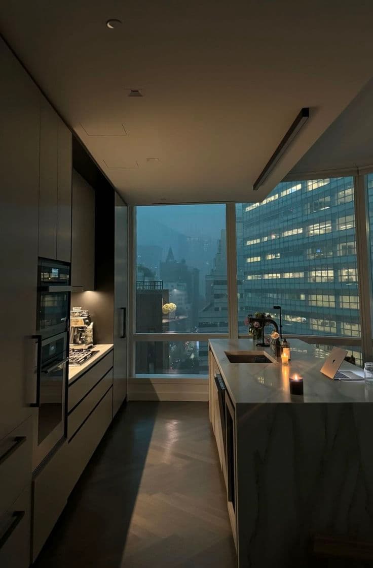 an empty kitchen with large windows overlooking the city at night in the evening time,