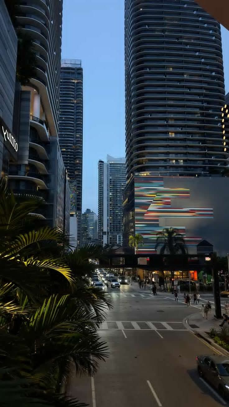 an empty city street with tall buildings and palm trees in the foreground at dusk