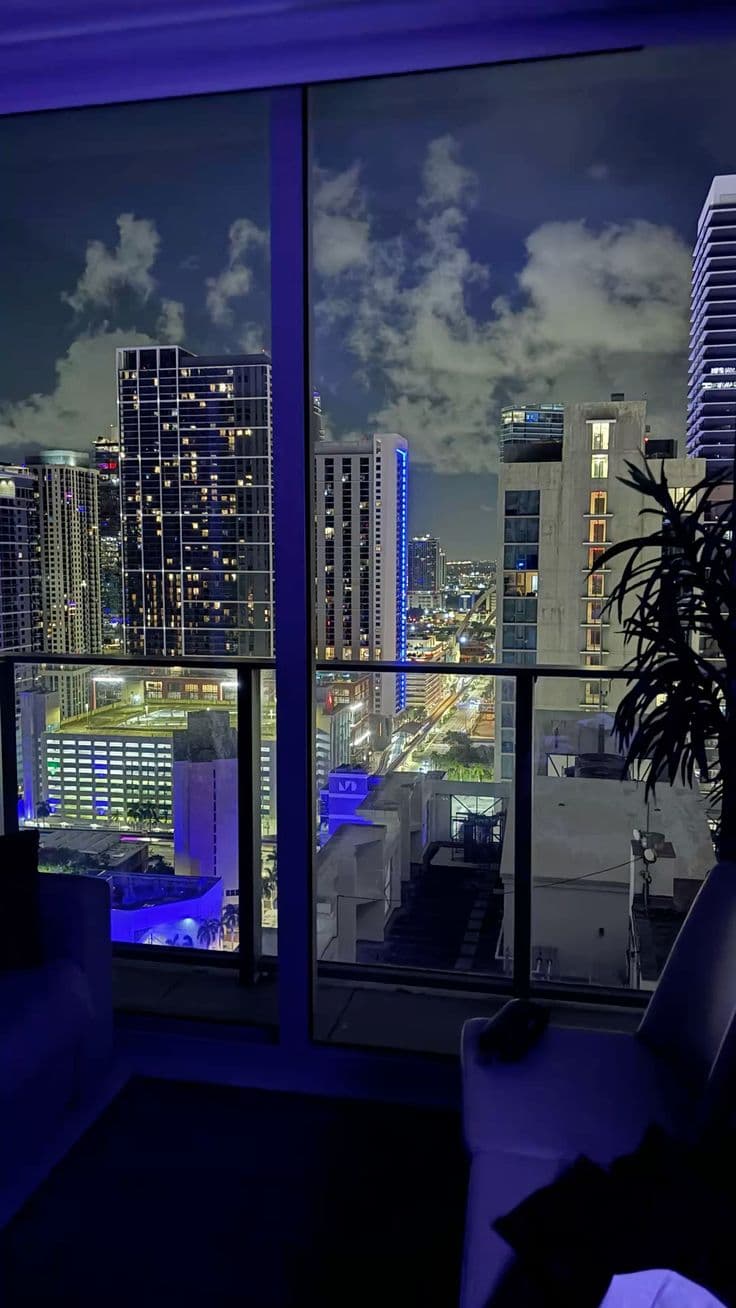 a living room filled with furniture and a large window overlooking the city at night time