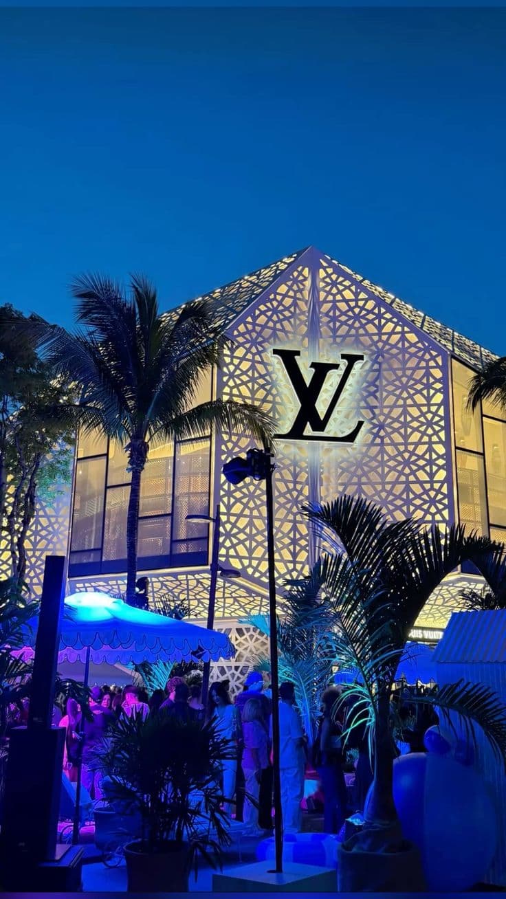 a building with palm trees in front of it and people walking around outside at night