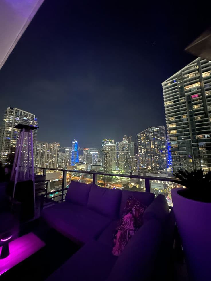 purple couches on the roof of a high rise building with city lights in the background