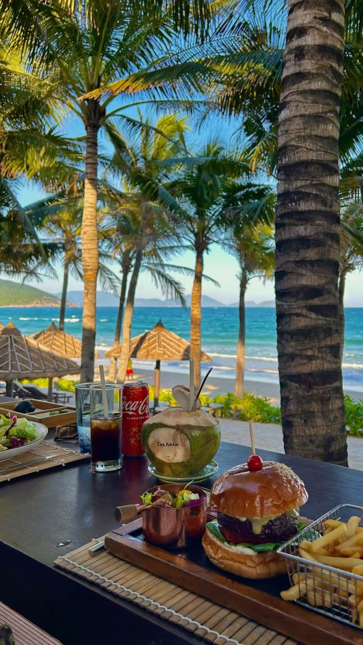 a table with food and drinks on it next to the beach in front of palm trees