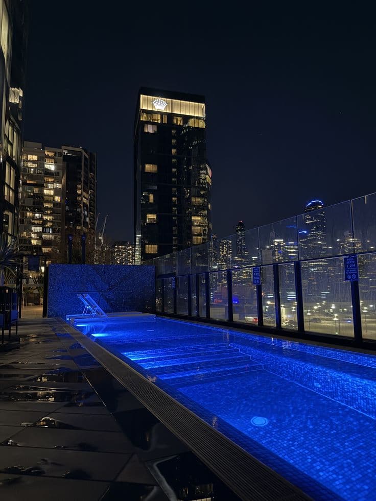 an empty swimming pool in the middle of a city at night with skyscrapers lit up