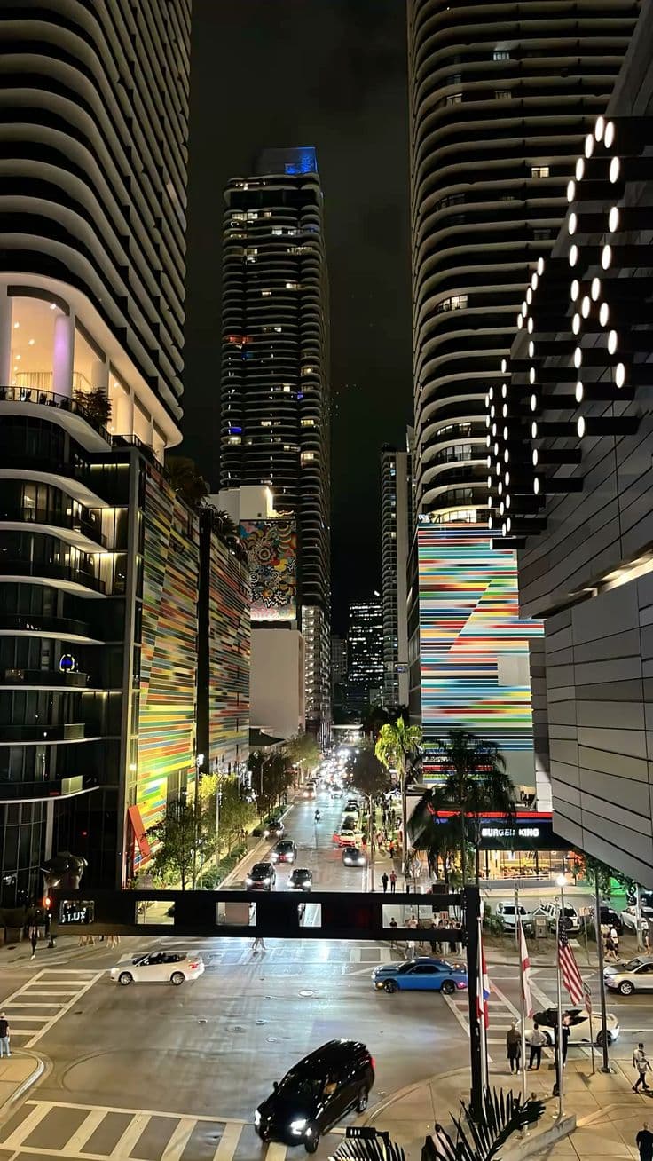 a city street at night with tall buildings and cars driving down it's sides