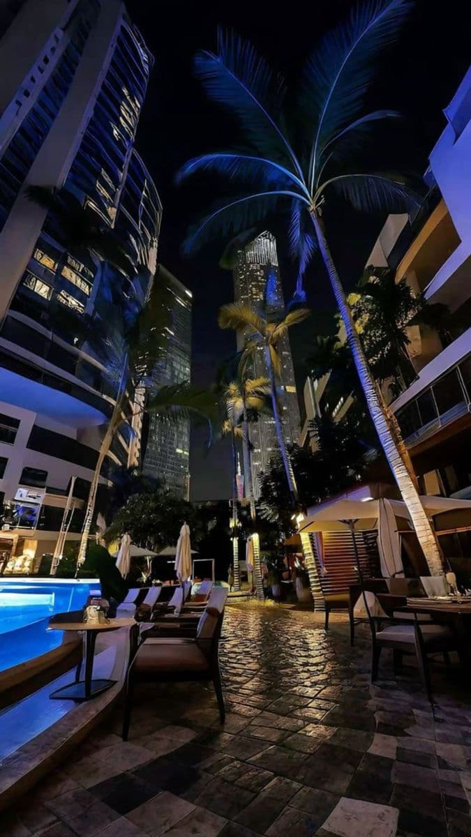 an outdoor swimming pool surrounded by palm trees and tall buildings in the background at 