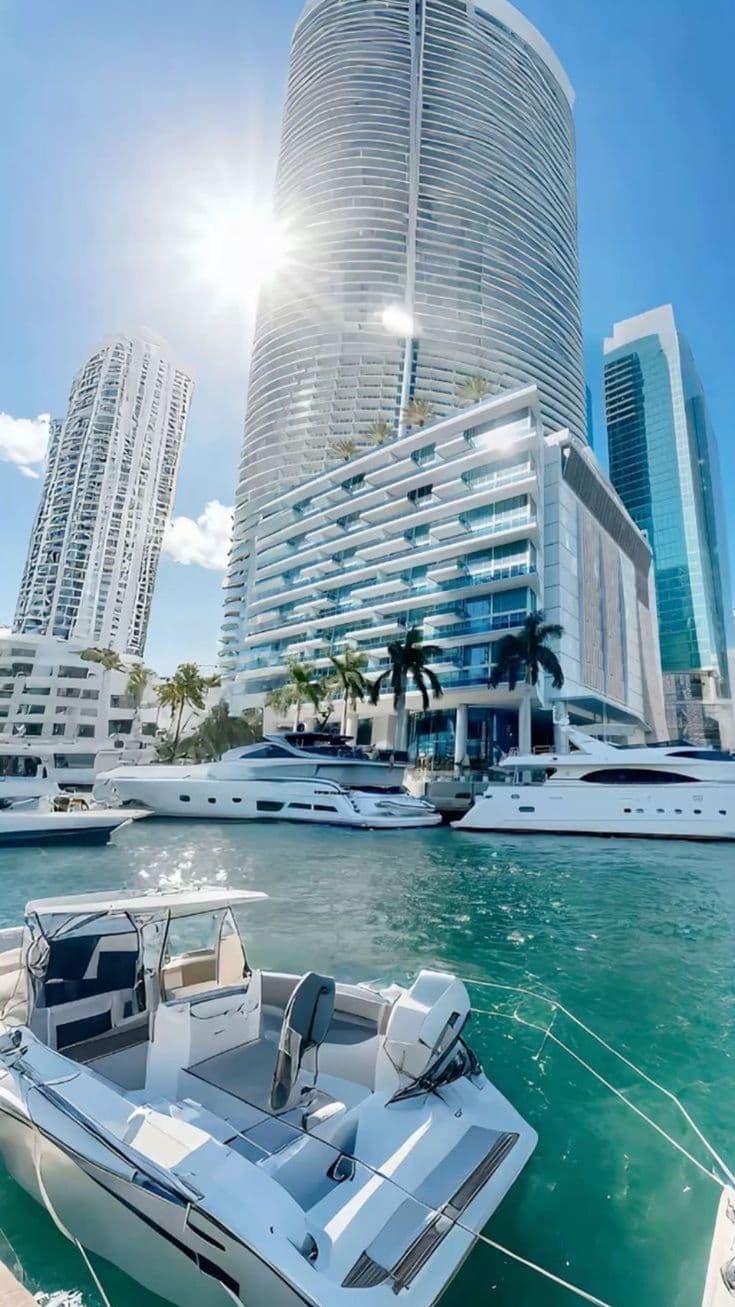 boats are parked in the water near some tall buildings and palm trees on the other side