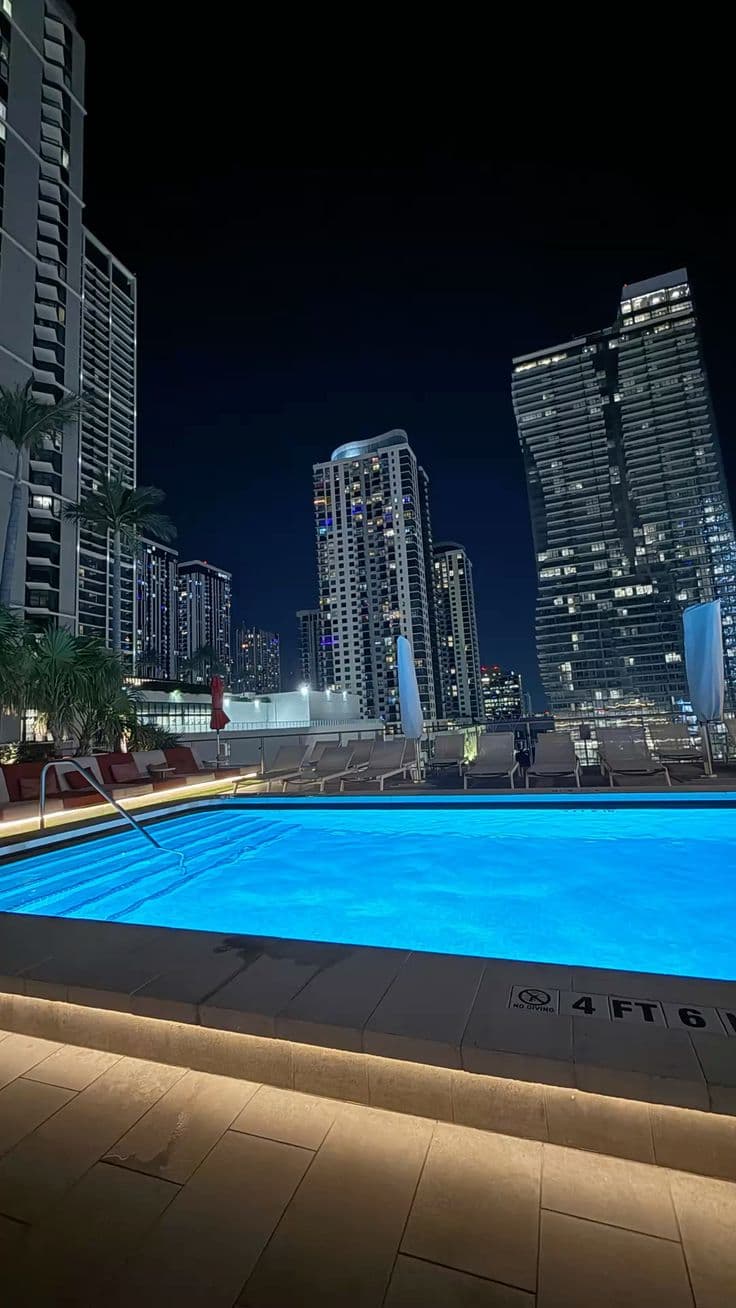 an empty swimming pool in the middle of a city at night with skyscrapers behind it
