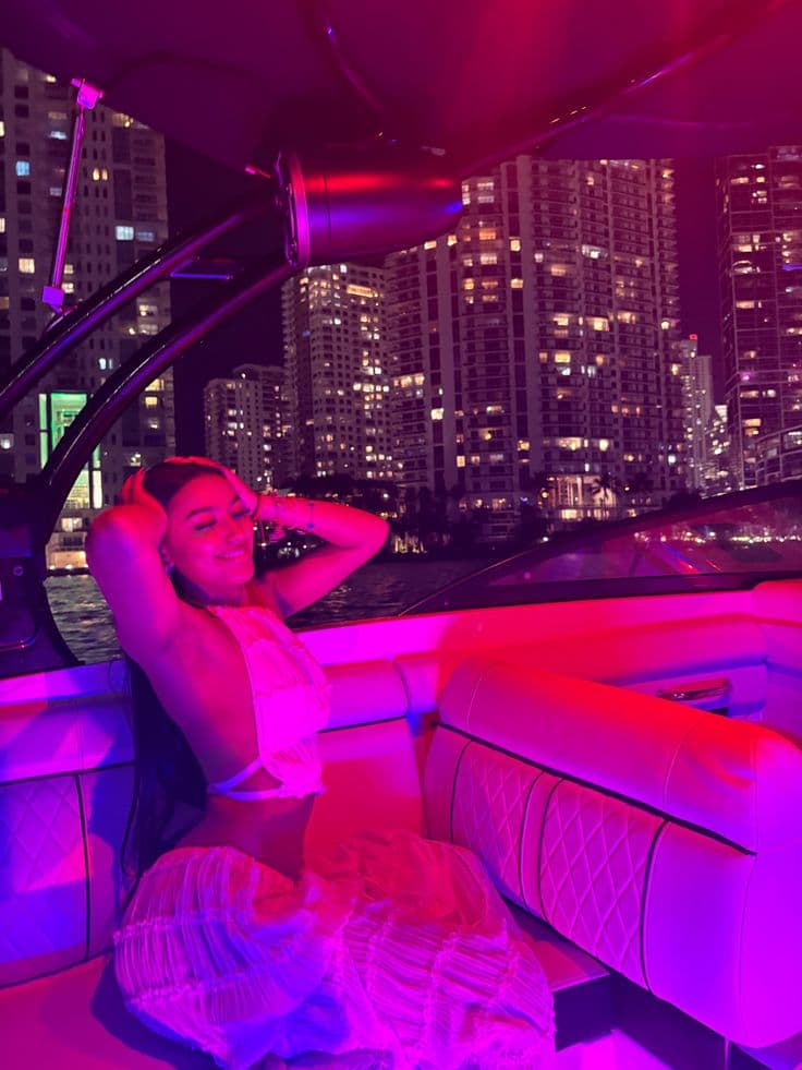 a woman sitting on the back of a boat in front of a city at night