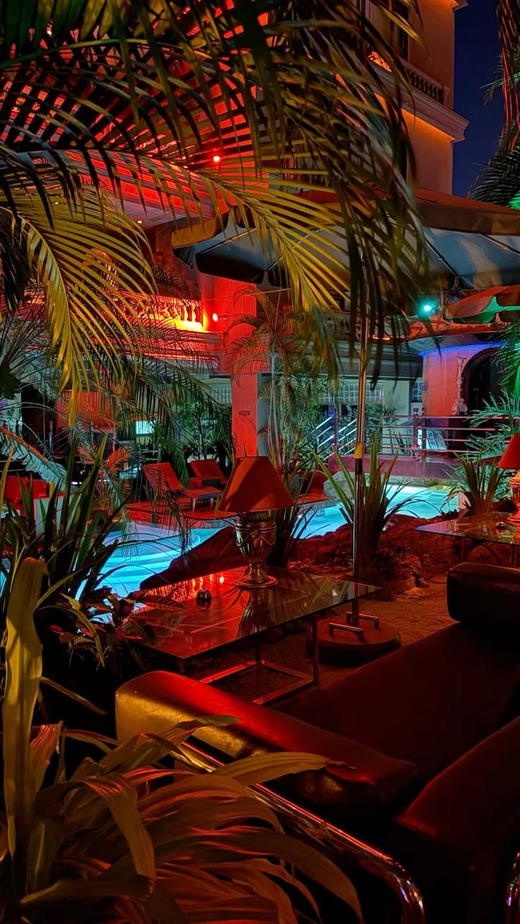 an indoor swimming pool surrounded by palm trees and other greenery in the evening time