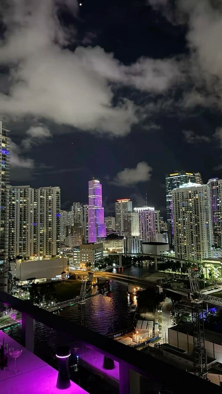 the city skyline is lit up at night with purple lights and clouds in the sky