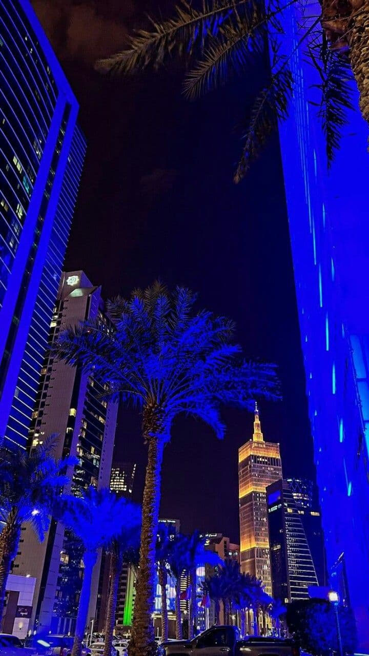 palm trees and skyscrapers lit up at night in an urban area with blue lighting