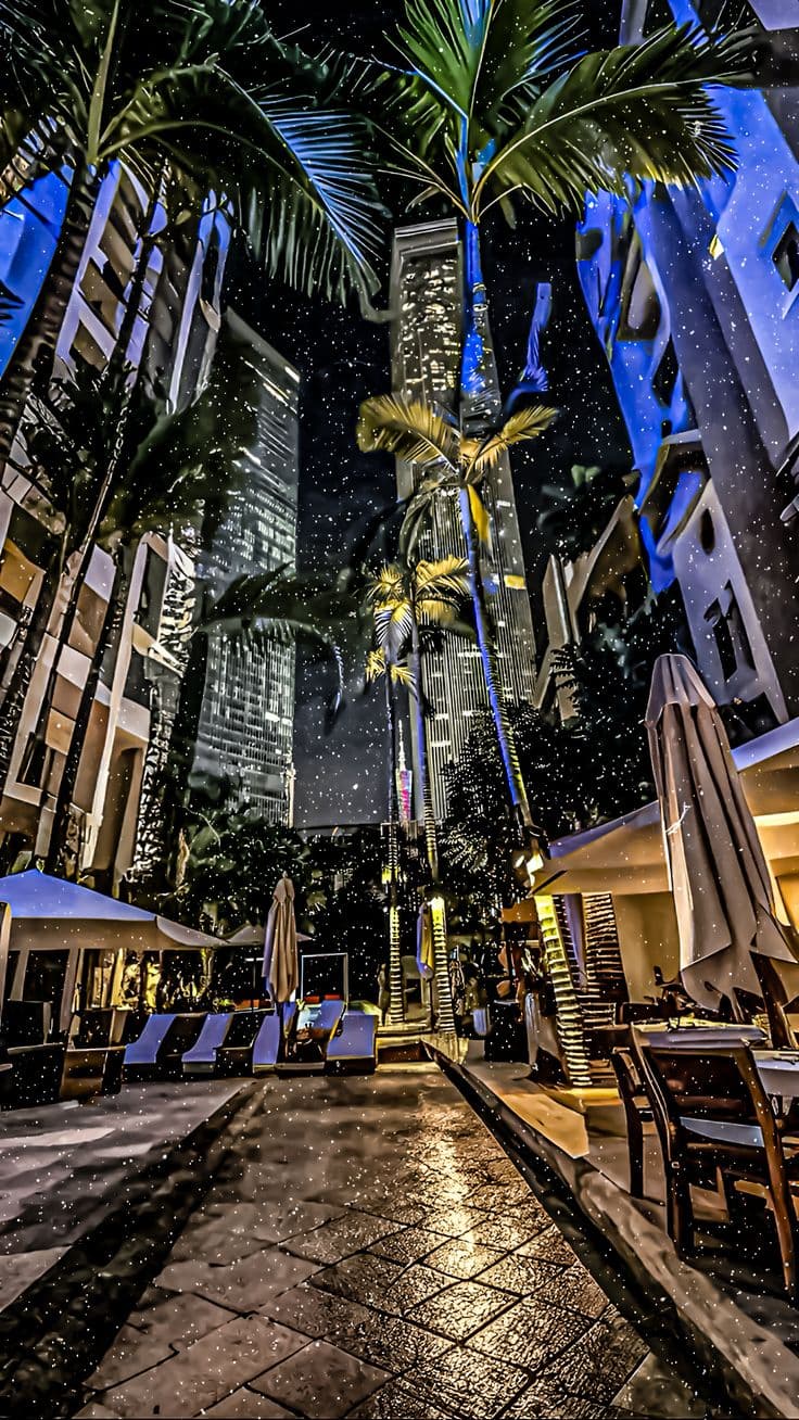 a city street with palm trees and buildings in the background at night, lit up by bright l