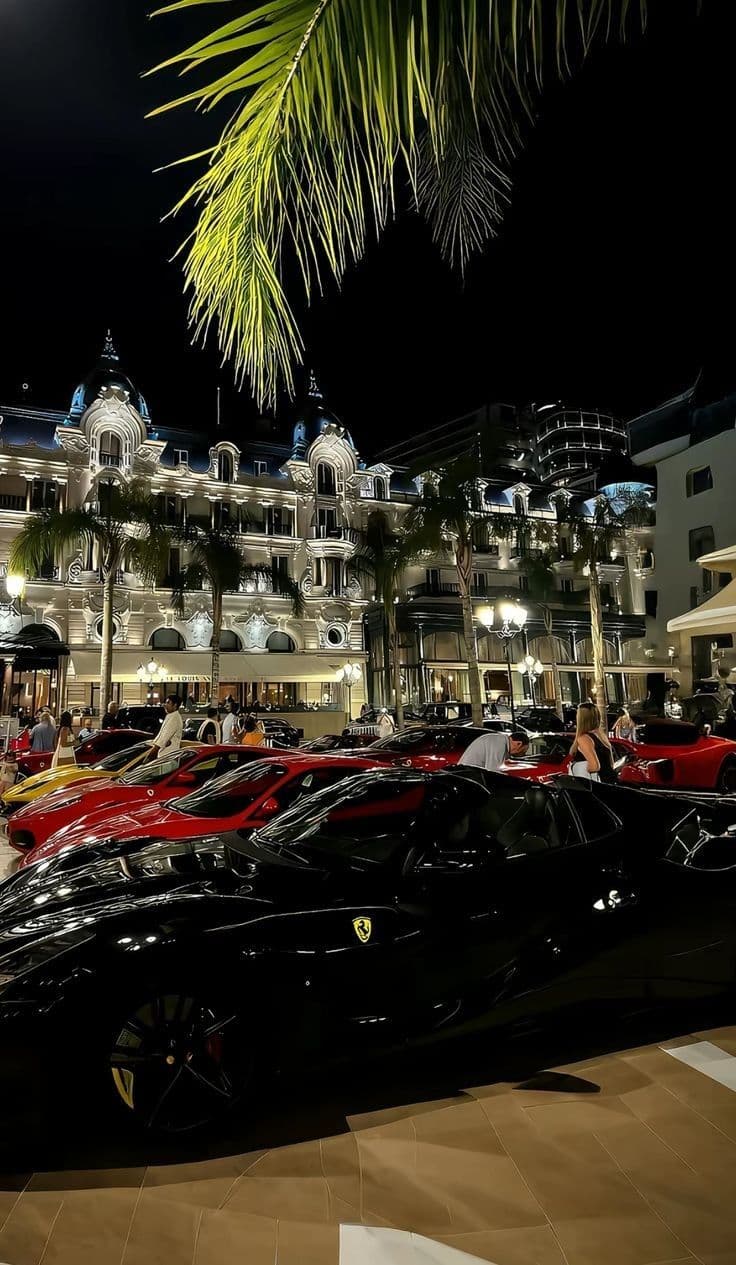 a bunch of cars parked in front of a building at night time with palm trees