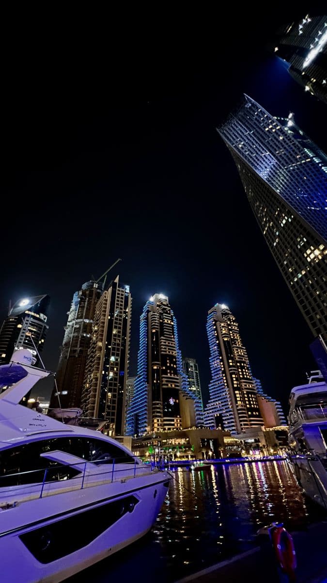 boats are docked in the water near tall buildings and skyscrapers lit up at night