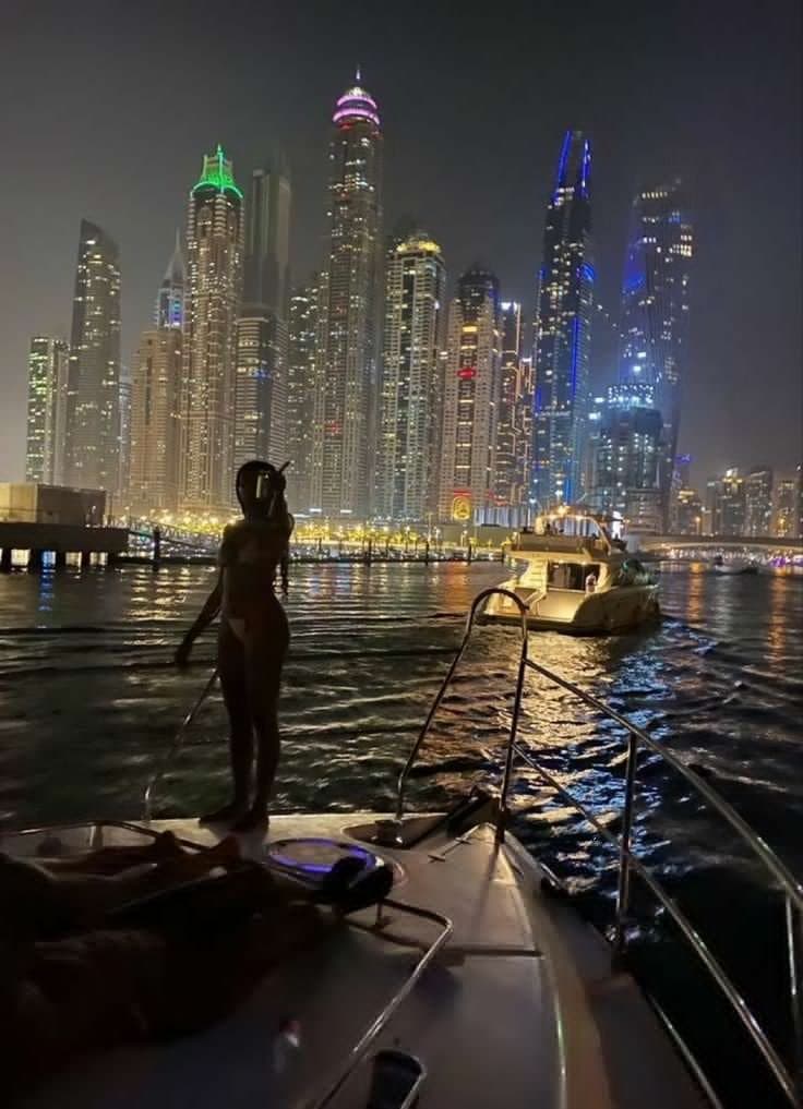a woman standing on the bow of a boat in front of a cityscape
